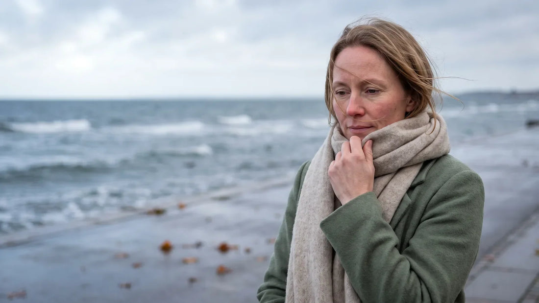 Kvinde med rosacea-rødme trækker halstørklædet op mod efterårsvinden ved den danske kyst